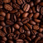 Café nas refeições e seus efeitos na saúde "Close-up de grãos de café torrado, com textura rica e cor marrom intensa. A imagem representa o consumo de café durante ou após as refeições – um hábito comum que pode impactar a absorção de nutrientes, a digestão e a saúde gastrointestinal. Ideal para conteúdos sobre nutrição, saúde digestiva e hábitos alimentares."